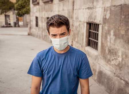 Young sad desperate man wearing surgical face mask in public spaces. Man with protective mask walking outdoors city street after coronavirus outbreak lockdown. New Normal life and COVID-19.の写真素材