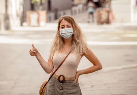 Young woman wearing protective face mask outdoors in city street. Positive image of New Normal life after COVID-19 and health protocols to avoid infections and the virus spread in public spaces.の写真素材