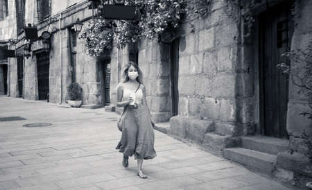 Young woman in city street wearing protective face mask and using mobile phone video calling or on video conference. The New Normal, technology and use of face mask to protect against coronavirus.の写真素材