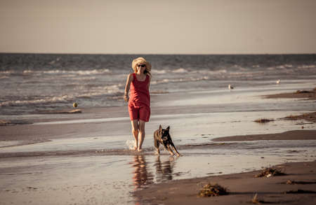 Beautiful mature retired woman and pet dog walking together on empty remote beach. In Outdoors exercise Hope and back to new normal life after Coronavirus lockdown concept.の写真素材