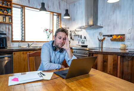 Stressed business man on laptop working from home looking worried, tired and overwhelmed. Exhausted entrepreneur working remotely during social distancing. Mental health and coronavirus lockdown.の写真素材