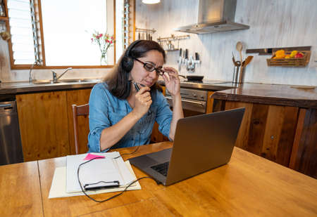 Stressed business woman working from home on laptop looking worried, tired and overwhelmed. Exhausted female working remotely during social distancing. Mental health and coronavirus lockdown.の写真素材