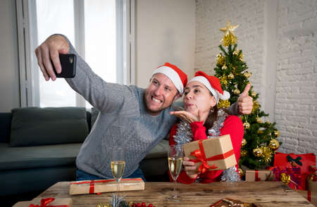 Happy couple video calling friends with mobile cell phone celebrating Virtual christmas and New year in lockdown. Virtual celebrations, social distancing during winter holidays due to COVID-19.の写真素材