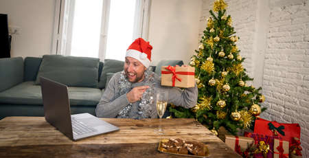 Happy man home alone in lockdown celebrating virtual christmas using laptop video calling family and...