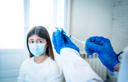 Nurse administering the vaccine to a young girl patient with face mask in Doctors clinic....
