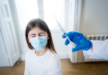 Nurse administering the vaccine to a young girl patient with face mask in Doctors clinic. Immunization, medical treatmentの写真素材