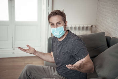 Sad man with protective face mask at home living room couch feeling tired and worried suffering...