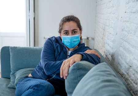Sad latin woman with protective face mask at home living room couch feeling tired and worried...