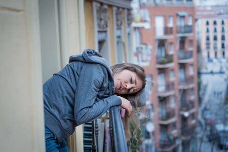 Beautiful depressed lonely woman staring out feeling sad, pain, grief on a balcony at home. Crisis,...
