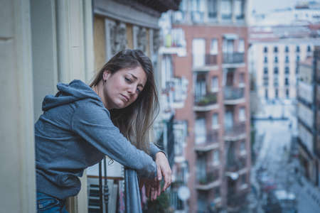 Young caucasian sad and depressed woman standing on a balcony feeling stressed and overwhelmed....