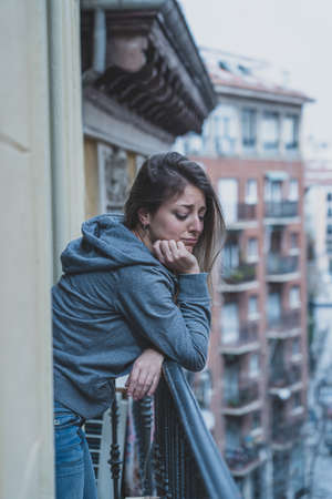 Young caucasian sad and depressed woman standing on a balcony feeling stressed and overwhelmed. Female suffering from depression in Mental Health conceptの写真素材