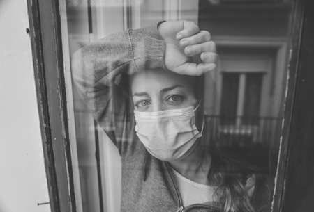 Young beautiful depressed unhappy caucasian woman looking worried and sad through the window at home. Feeling worthless and in pain. closeup. Depression and Mental Health conceptの写真素材