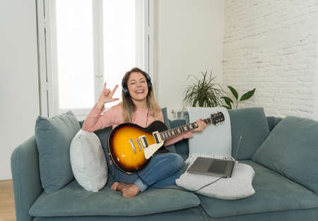Woman playing electric guitar with laptop in online music lesson. Female having fun watching video tutorial on learning rock songs. Hobbies and leisure, virtual activities during social distancing.の写真素材