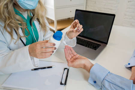 Young attractive caucasian woman doctor holding a jar of pills explaining prescription and medical...