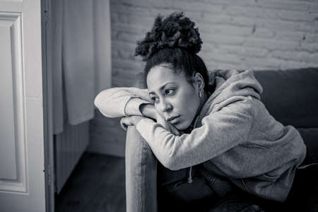 Unhappy lonely young african american woman suffering from anxiety, stress and depression feeling alone and distressed at home. Mental health and social isolation among young people concept.の写真素材