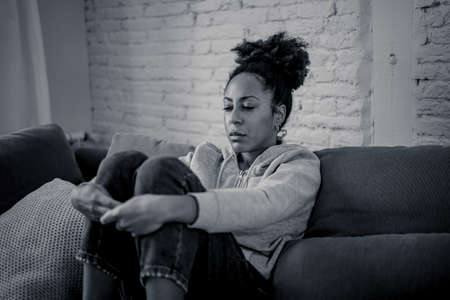 Unhappy lonely young african american woman suffering from anxiety, stress and depression feeling alone and distressed at home. Mental health and social isolation among young people concept.の写真素材