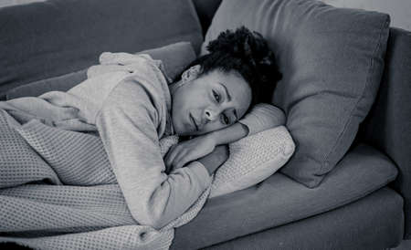 Unhappy lonely young african american woman suffering from anxiety, stress and depression feeling alone and distressed at home. Mental health and social isolation among young people concept.の写真素材