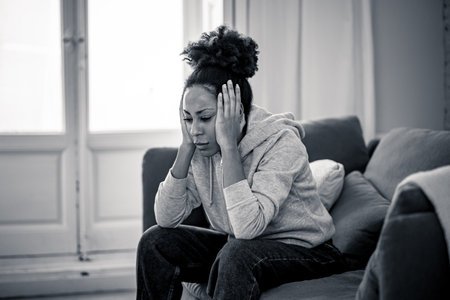 Unhappy lonely young african american woman suffering from anxiety, stress and depression feeling alone and distressed at home. Mental health and social isolation among young people concept.の写真素材