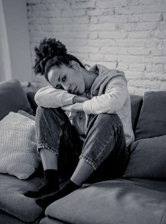 Unhappy lonely young african american woman suffering from anxiety, stress and depression feeling alone and distressed at home. Mental health and social isolation among young people concept.の写真素材