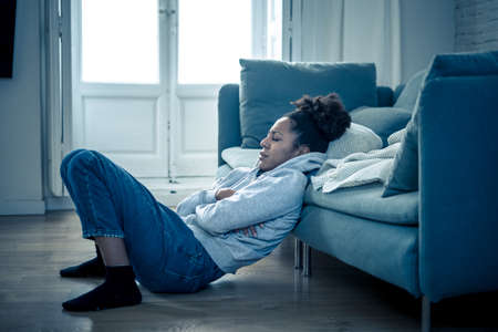 Depressed african woman with sad expression, headache and depression feeling desperate at home. Afro American teen or Attractive black young female lying thoughtful and sick on sofa in pain and worry.の写真素材