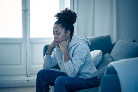 Depressed african woman with sad expression, headache and depression feeling desperate at home. Afro American teen or Attractive black young female lying thoughtful and sick on sofa in pain and worry.の写真素材