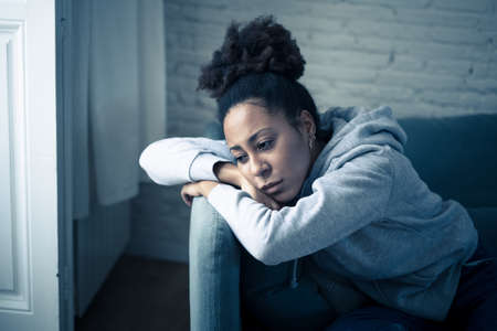 Depressed african woman with sad expression, headache and depression feeling desperate at home. Afro American teen or Attractive black young female lying thoughtful and sick on sofa in pain and worry.の写真素材