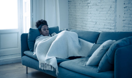 Depressed African woman with sad expression, headache and depression feeling desperate at home. Afro American, Attractive black young female lying thoughtful and sick on sofa in pain and worry.の写真素材