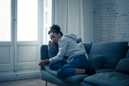 Depressed African woman with sad expression, headache and depression feeling desperate at home. Afro American, Attractive black young female lying thoughtful and sick on sofa in pain and worry.の写真素材