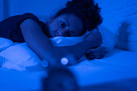 Young beautiful afro american woman at home lying in bed late at night trying to sleep suffering insomnia sleeping disorder or scared on nightmares looking stressed and worried Mental health concept.の写真素材