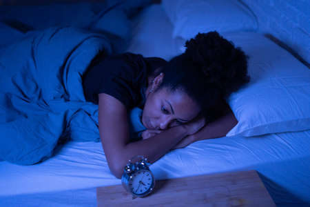 Young beautiful afro american woman at home lying in bed late at night trying to sleep suffering insomnia sleeping disorder or scared on nightmares looking stressed and worried Mental health concept.の写真素材