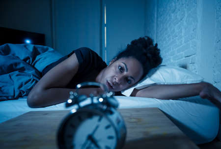 Young beautiful afro american woman at home lying in bed late at night trying to sleep suffering insomnia sleeping disorder or scared on nightmares looking stressed and worried Mental health concept.の写真素材
