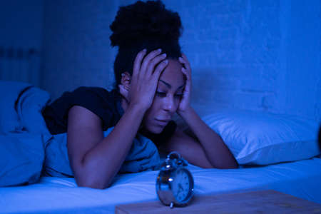 Young beautiful afro american woman at home lying in bed late at night trying to sleep suffering insomnia sleeping disorder or scared on nightmares looking stressed and worried Mental health concept.の写真素材