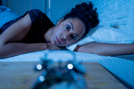Young beautiful afro american woman at home lying in bed late at night trying to sleep suffering insomnia sleeping disorder or scared on nightmares looking stressed and worried Mental health concept.の写真素材