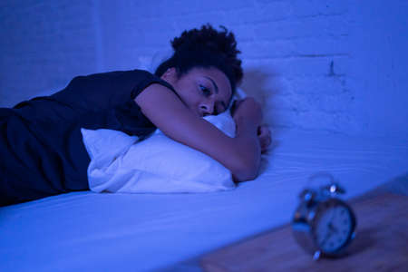 Young beautiful afro american woman at home lying in bed late at night trying to sleep suffering insomnia sleeping disorder or scared on nightmares looking stressed and worried Mental health concept.の写真素材