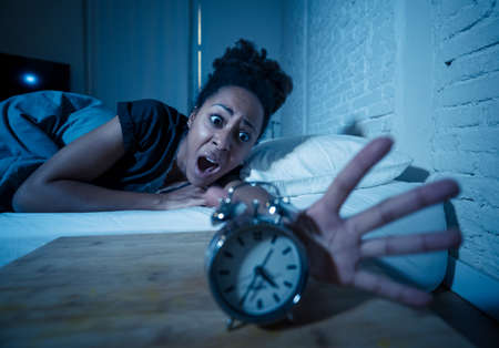 Young beautiful afro american woman at home lying in bed late at night trying to sleep suffering insomnia sleeping disorder or scared on nightmares looking stressed and worried Mental health concept.の写真素材
