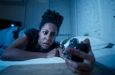 Young beautiful afro american woman at home lying in bed late at night trying to sleep suffering insomnia sleeping disorder or scared on nightmares looking stressed and worried Mental health concept.の写真素材