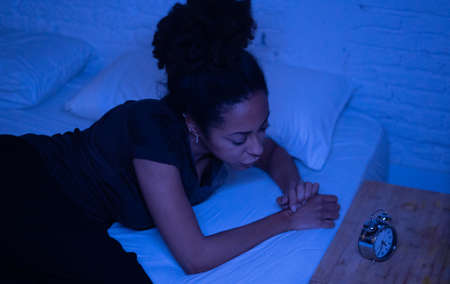 Young beautiful afro american woman at home lying in bed late at night trying to sleep suffering insomnia sleeping disorder or scared on nightmares looking stressed and worried Mental health concept.の写真素材