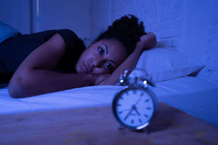 Young beautiful afro american woman at home lying in bed late at night trying to sleep suffering insomnia sleeping disorder or scared on nightmares looking stressed and worried Mental health concept.の写真素材