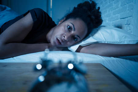 Young beautiful afro american woman at home lying in bed late at night trying to sleep suffering insomnia sleeping disorder or scared on nightmares looking stressed and worried Mental health concept.の写真素材