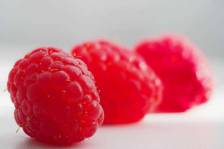 three raspberries in a row, focus on the first, three red-pink raspberries on a white table,...