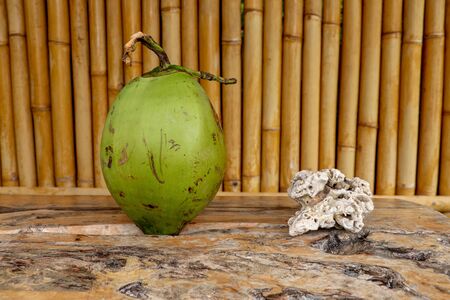 Fresh young coconut on table with massive wooden board. Young Coconut Fruit for Drink Sweet Juice and Eat. Healthy natural refreshment full of energy and vitamins. In the background wall of bamboo.の写真素材
