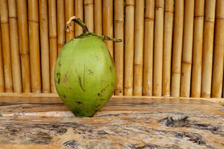 Fresh young coconut on table with massive wooden board. Young Coconut Fruit for Drink Sweet Juice and Eat. Healthy natural refreshment full of energy and vitamins. In the background wall of bamboo.の写真素材