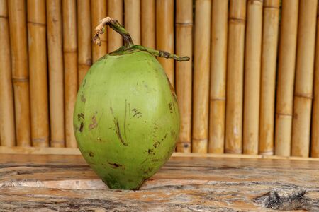 Fresh young coconut on table with massive wooden board. Young Coconut Fruit for Drink Sweet Juice and Eat. Healthy natural refreshment full of energy and vitamins. In the background wall of bamboo.の写真素材