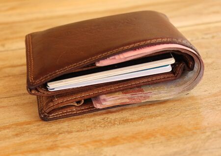 Brown leather wallet full of banknotes and credit cards. Men's wallet on a wooden table. Money in a closed brown purse. Best background for your project.の写真素材
