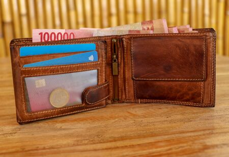 Brown leather wallet full of banknotes and credit cards. Men's wallet on a wooden table. Money in a...
