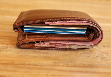Brown leather wallet full of banknotes and credit cards. Men's wallet on a wooden table. Money in a closed brown purse. Best background for your project.の写真素材