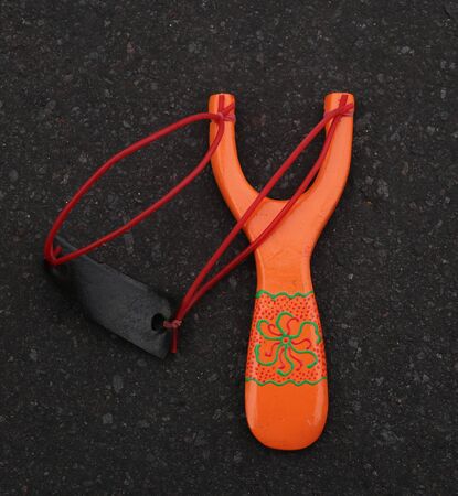 Handmade orange slingshot catapult. Y-shaped wooden stick with elastic tied between two top parts. Slingshot or Catapult is a device for shooting small stones.の写真素材