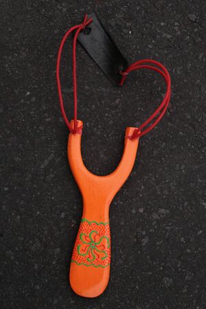 Handmade orange slingshot catapult. Y-shaped wooden stick with elastic tied between two top parts. Slingshot or Catapult is a device for shooting small stones.の写真素材