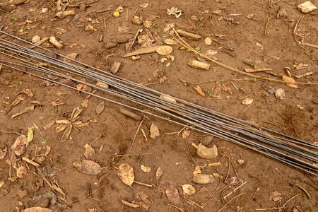 Steel rebar for reinforcement concrete at construction site with house under construction background. Steel wires laid on clay ground with dry leaves. Straight wires ready for construction.の写真素材