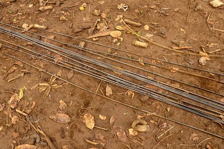 Steel rebar for reinforcement concrete at construction site with house under construction background. Steel wires laid on clay ground with dry leaves. Straight wires ready for construction.の写真素材